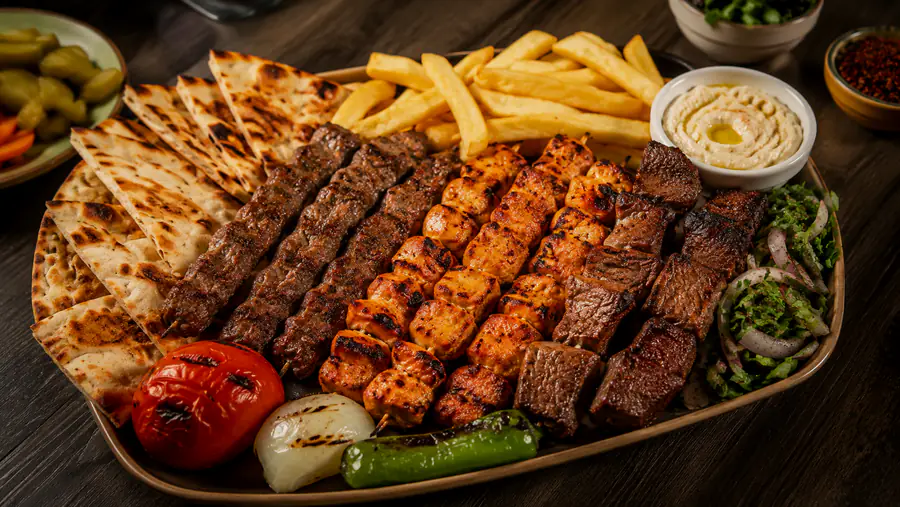 صحن مشاوي يضم الكباب وشيش الطاووق وقطع اللحم المشوية، مع الخبز والطماطم والبصل المشوي.